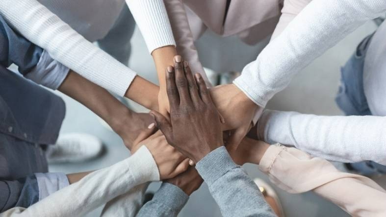 a multicultural set of hands in a huddle. the hands are piled one on top of another